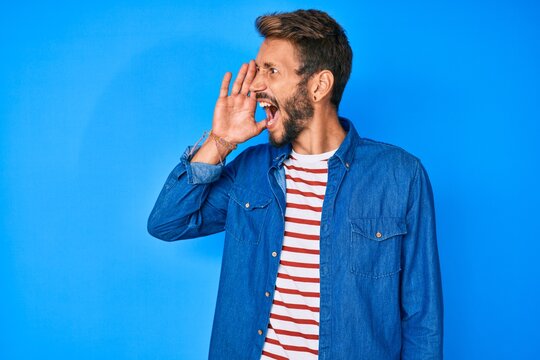 Handsome caucasian man with beard wearing casual clothes shouting and screaming loud to side with hand on mouth. communication concept.