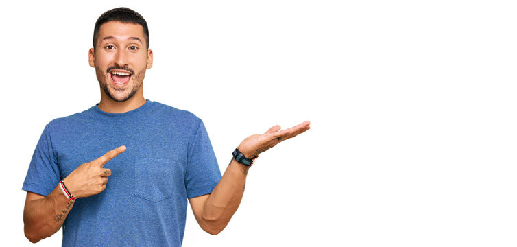 Handsome man with tattoos wearing casual clothes amazed and smiling to the camera while presenting with hand and pointing with finger.