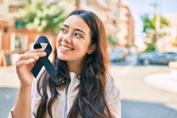 Young hispanic woman smiling happy holding black ribbon at the city.