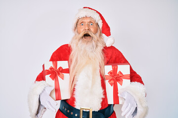 Old senior man wearing santa claus costume holding presents celebrating crazy and amazed for success with open eyes screaming excited.