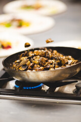 Professional hotel chef is sautéing mushrooms in a pan.

