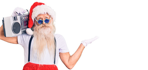 Old senior man with grey hair and long beard wearing santa claus costume and boombox celebrating victory with happy smile and winner expression with raised hands