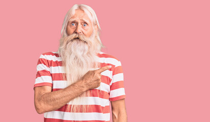 Old senior man with grey hair and long beard wearing striped tshirt pointing aside worried and...