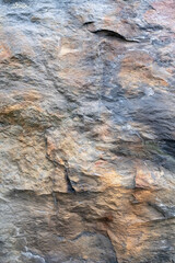 Multicolored rock wall. Stone textured surface close-up. Copy space. Abstract natural background. Vertical photo.