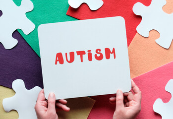 World Autism Awareness Day. Jigsaw puzzle on felt. Hands hold cardboard placard with text Autism..