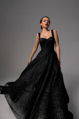 Full length studio fashion portrait. Elegant woman in black shiny evening dress. Dynamic shot....