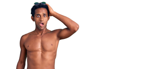 African handsome man wearing swimsuit and sunglasses surprised with hand on head for mistake,...