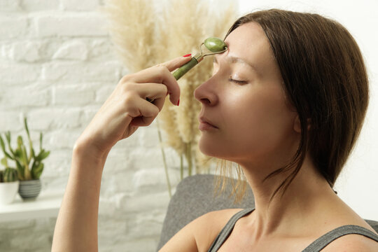 Face massage. Woman using jade face roller for skin care. Home spa concept.