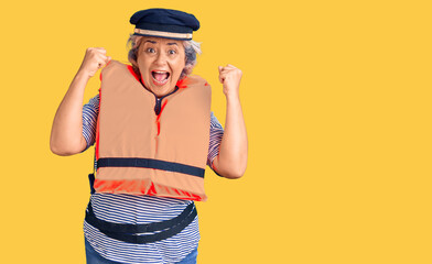 Senior woman with gray hair wearing nautical lifejacket screaming proud, celebrating victory and success very excited with raised arms