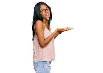 Young african american woman wearing casual clothes and glasses pointing aside with hands open palms showing copy space, presenting advertisement smiling excited happy