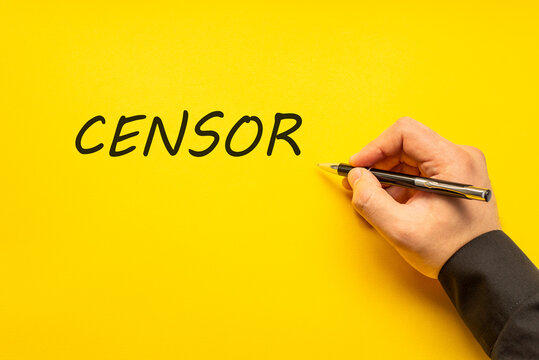 Male hand writes in black pen the word censor on a yellow background with copy space. Business concept photo