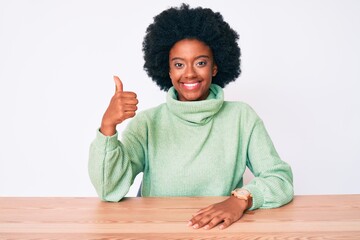 Young african american woman wearing casual winter sweater smiling happy and positive, thumb up doing excellent and approval sign