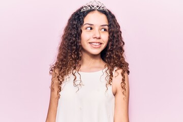 Beautiful kid girl with curly hair wearing princess tiara looking to side, relax profile pose with natural face and confident smile.