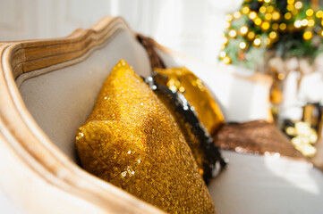 Gold shining decorative pillow with sequins on a beige sofa, garland and bokeh on Christmas interior on background, . Christmas decor for the home.