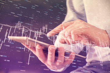 Double exposure of man's hands holding and using a digital device and forex graph drawing. Financial market concept.