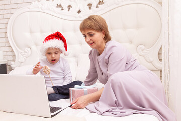 A boy with Down syndrome and a disability sits with his mother on the couch, online video greetings...