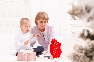 A boy with Down syndrome and a disability sits with his mother on the couch, online video greetings...