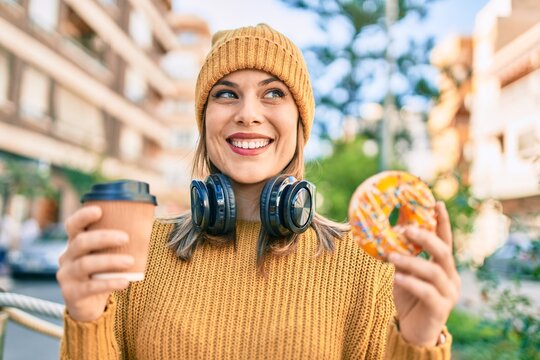 Young blonde woman using headphones and having breakfast at the city.