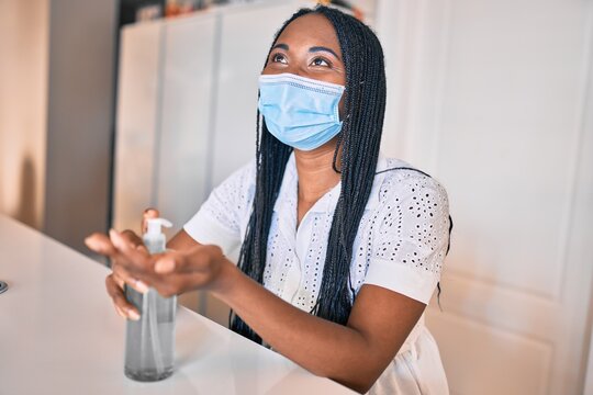 Young african american woman wearing medical mask using sanitizer hand gel at home