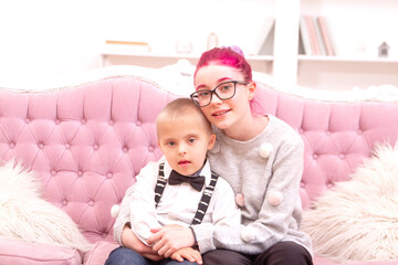 A boy and a girl are sitting on the couch by the Christmas tree, the boy has Down Syndrome, the...