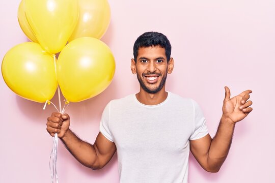 Young latin man holding balloons smiling happy pointing with hand and finger to the side