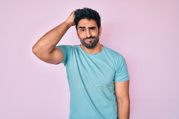 Handsome hispanic man with beard wearing casual clothes confuse and wonder about question. uncertain with doubt, thinking with hand on head. pensive concept.