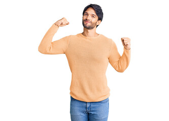 Handsome hispanic man wearing casual sweater showing arms muscles smiling proud. fitness concept.