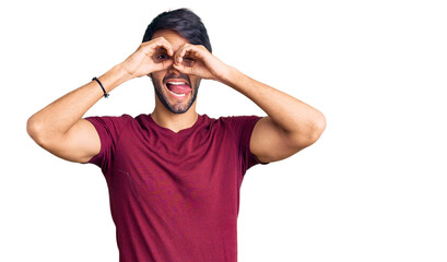 Handsome hispanic man wearing casual clothes doing ok gesture like binoculars sticking tongue out, eyes looking through fingers. crazy expression.