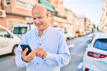 Middle age bald man smiling happy using smartphone at the city.