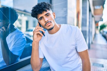 Young arab man with serious expression talking on the smartphone leaning on the wall.