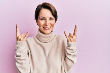 Young brunette woman with short hair wearing casual winter sweater shouting with crazy expression doing rock symbol with hands up. music star. heavy concept.