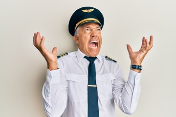 Handsome middle age mature man wearing airplane pilot uniform crazy and mad shouting and yelling with aggressive expression and arms raised. frustration concept. © Krakenimages.com