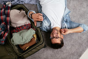 Young smiling man packing clothes into travel bag. Man preparing for the trip..