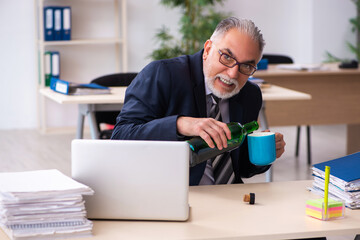 Old male employee drinking alcohol in the office