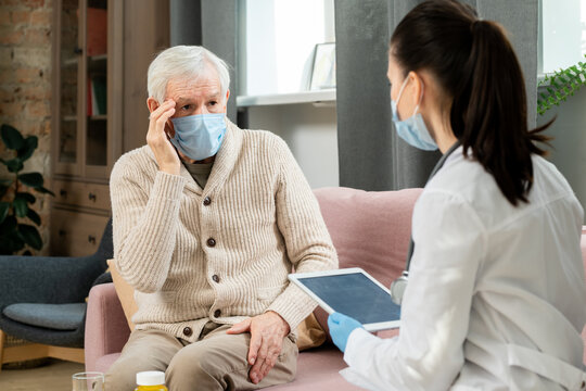 Sick senior man in protective medical mask complaining to doctor about headache