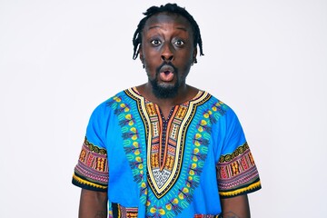 Young african american man with braids wearing traditional africa tshirt scared and amazed with open mouth for surprise, disbelief face