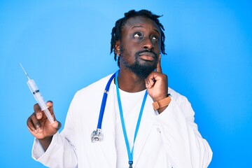 Young african american man with braids wearing doctor stethoscope holding syringe serious face thinking about question with hand on chin, thoughtful about confusing idea