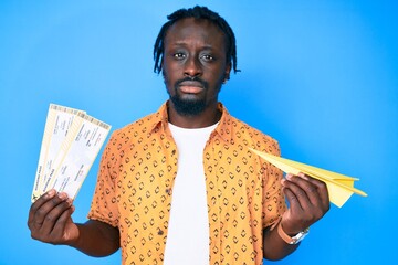 Young african american man with braids holding paper airplane and boarding pass relaxed with...