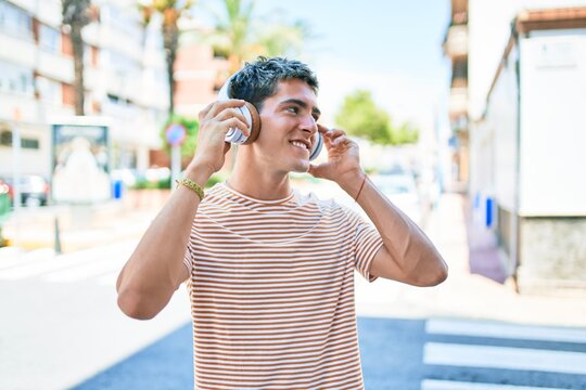 Young handsome caucasian man smiling happy listening to music using headphones walking at city.