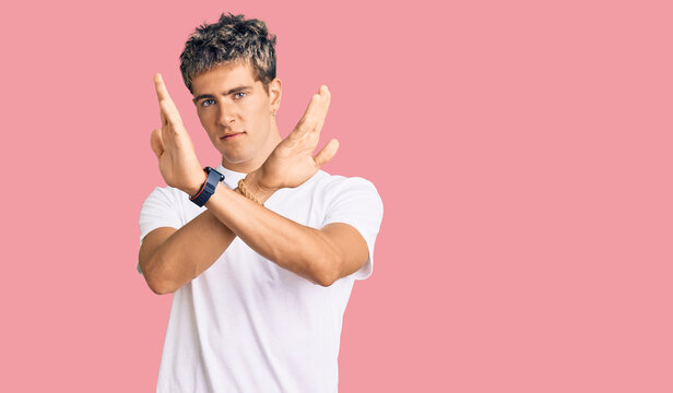 Young handsome man wearing casual white tshirt rejection expression crossing arms doing negative sign, angry face