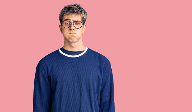 Young handsome man wearing casual clothes and glasses puffing cheeks with funny face. mouth inflated with air, crazy expression.