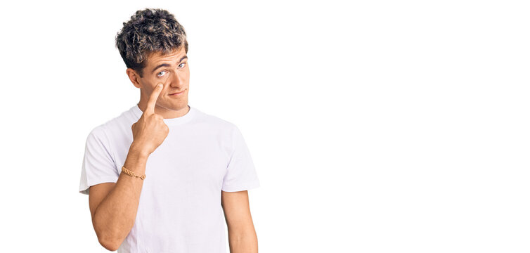 Young handsome man wearing casual white tshirt pointing to the eye watching you gesture, suspicious expression
