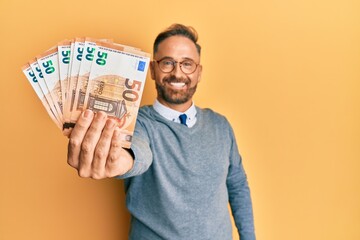 Handsome middle age man holding bunch of euros looking positive and happy standing and smiling with...