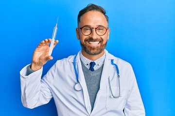 Handsome middle age man wearing doctor uniform holding syringe looking positive and happy standing and smiling with a confident smile showing teeth