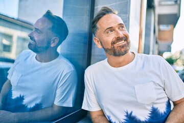 Middle age handsome man smiling happy leaning on the wall at the city.