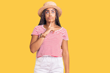 Young african american woman with braids wearing summer hat thinking concentrated about doubt with finger on chin and looking up wondering