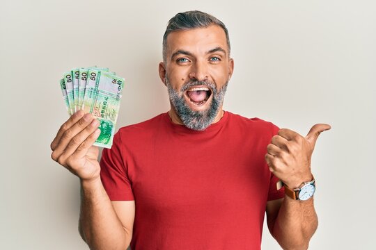 Middle age handsome man holding 50 hong kong dollars banknotes pointing thumb up to the side smiling happy with open mouth