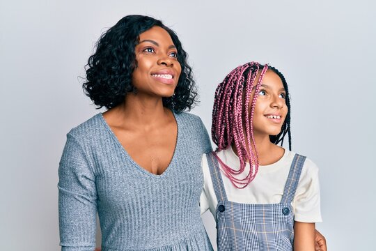 Beautiful african american mother and daughter wearing casual clothes and hugging looking away to side with smile on face, natural expression. laughing confident.