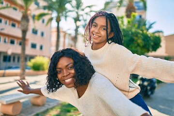 Beautiful african american mother giving daughter piggyback ride with open arms at the park.
