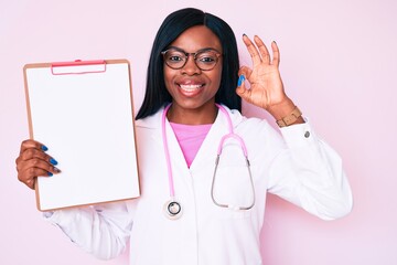 Young african american woman wearing doctor stethoscope holding clipboard doing ok sign with fingers, smiling friendly gesturing excellent symbol